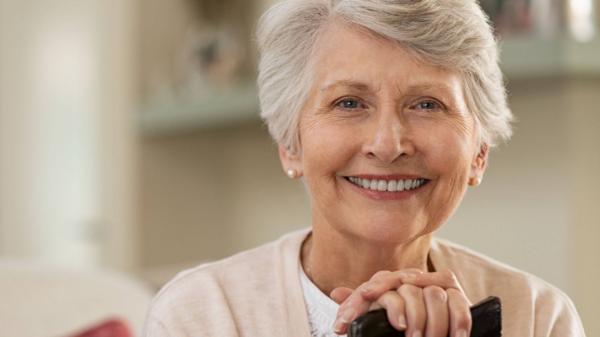 Older woman smiling and resting her hands on a walking cane